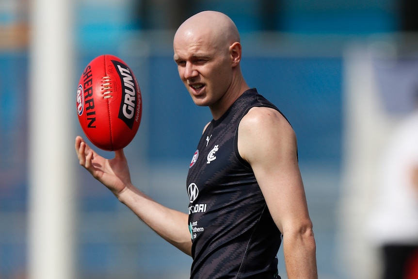 A Carlton AFL footballer throws a red ball in the air with his right hand at a training session.
