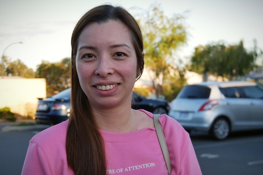 A woman in a pink shirt stands in a parking lot