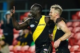 Two AFL teammates celebrate a goal, one raising his finger in salute, the other smiling.
