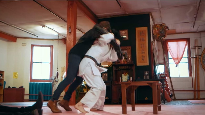 Izzi throwing a man over her shoulder at a martial arts dojo.