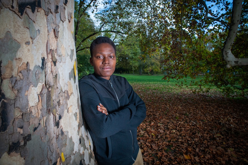 Negesa Annet leans against a tree with her arms folded and looks at the camera.
