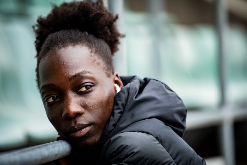 Bendere Oboya, wearing a puffy jacket and airpods, looks over her shoulder as she leans on a metal barrier.