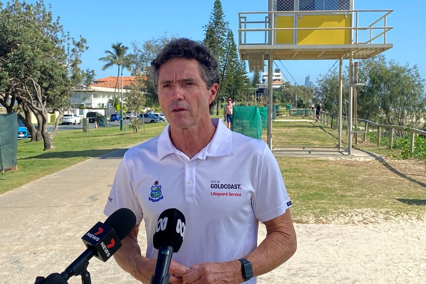 Man in white lifeguard shirt speaking into microphones in front of yellow lifesaver tower