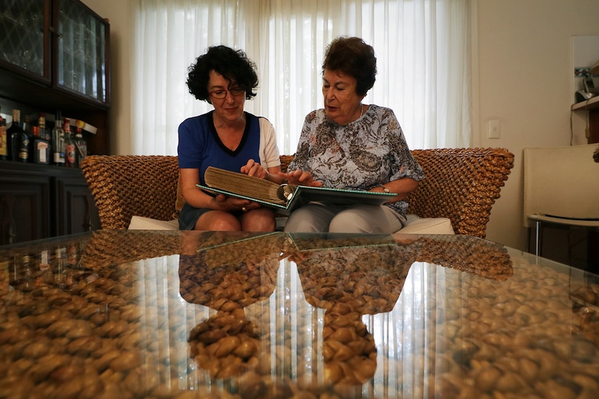 Two women sit on a sofa looking through a ring-bound photo album.