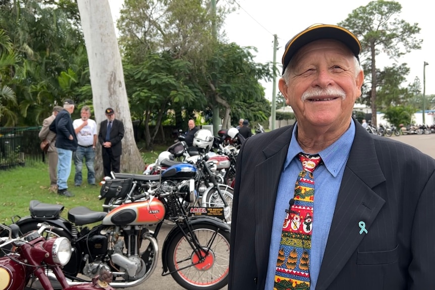 Man in bright tie smiles standing in front of motorbikes