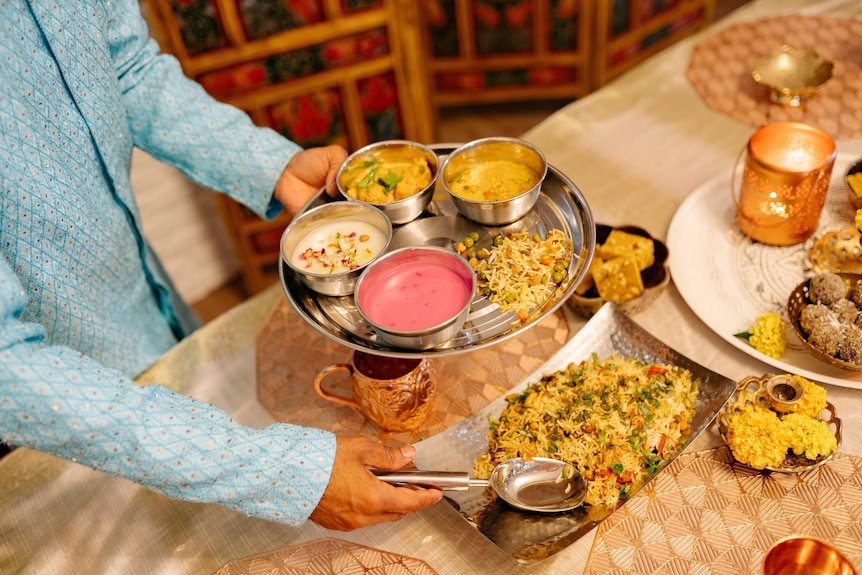 A person scooping some rice from a plate surrounded with multiple dishes