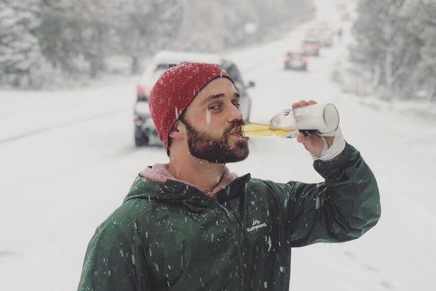 A man stands in the snow drinking a Corona.