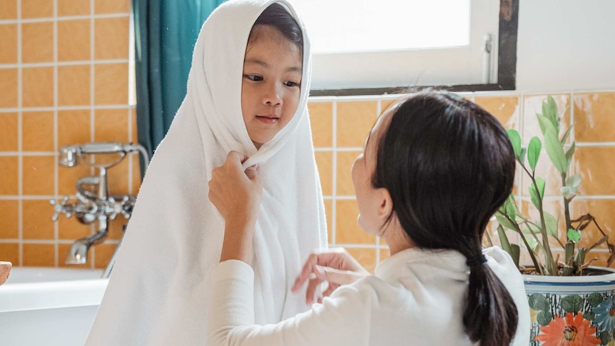A woman wraps a child in a white towel in a bathroom. For a story about teaching children correct names for their body parts.