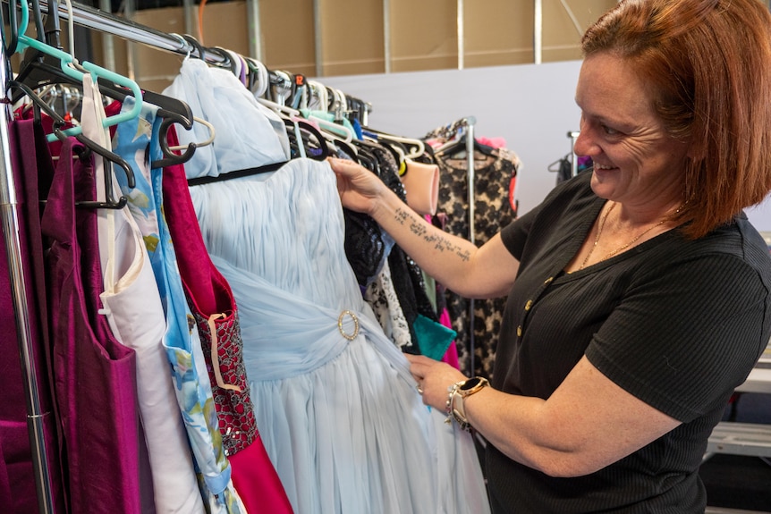 A woman with red hair looks at a powder blue layered gown. 