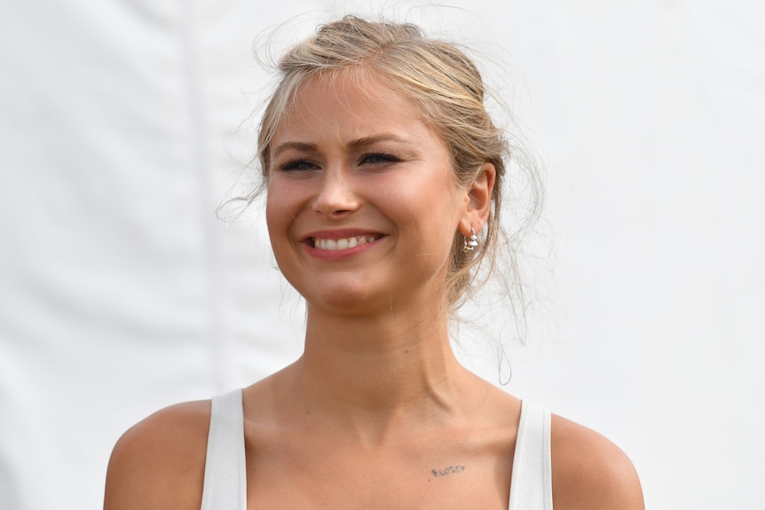 Australian of the Year Grace Tame smiling in front of a white background while wearing a white dress.