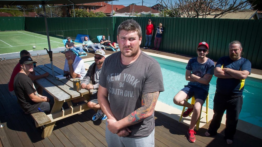 A small group of men sitting around a swimming pool and tennis court.