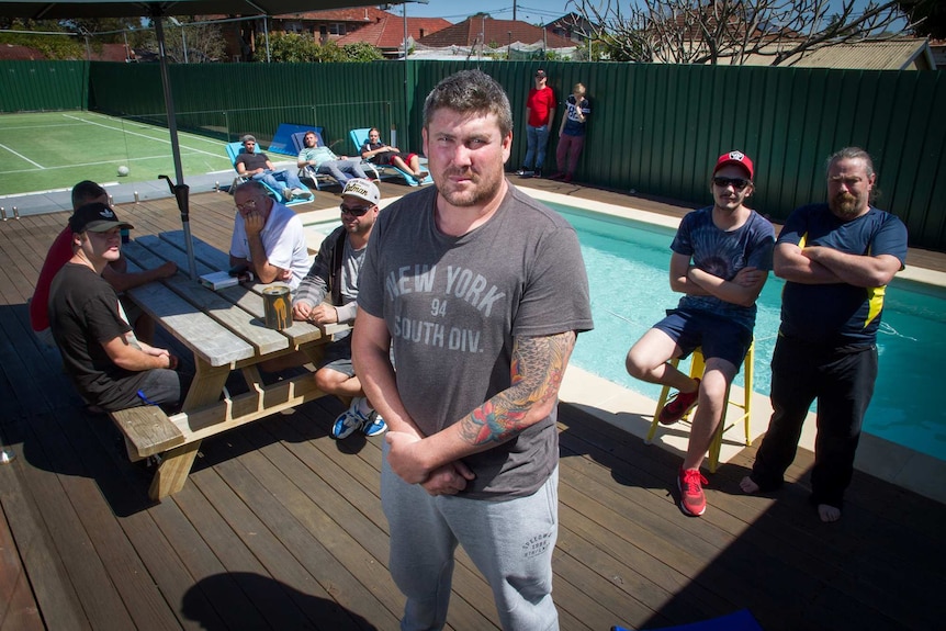 A small group of men sitting around a swimming pool and tennis court.