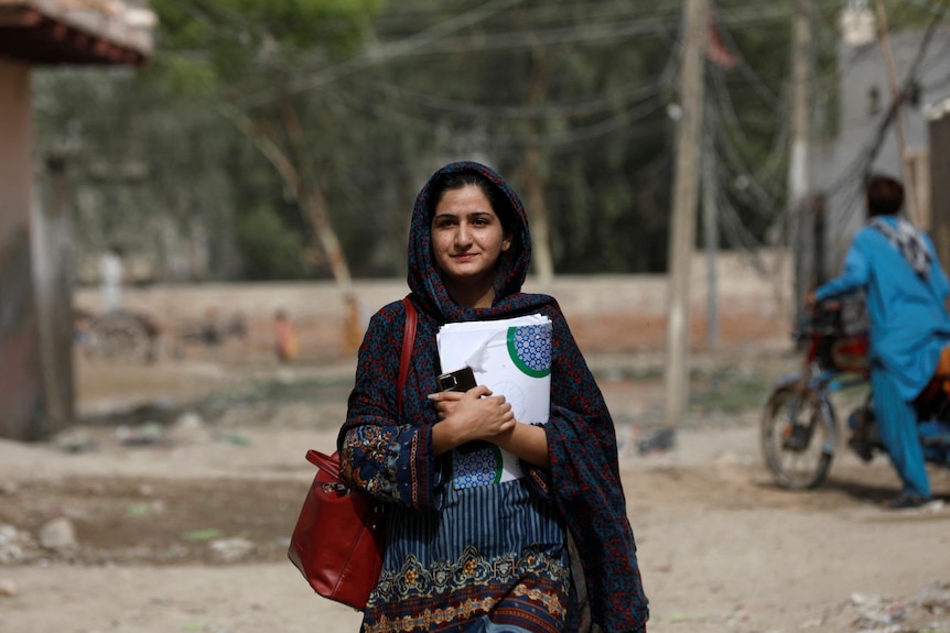 A young woman walking down holding her belongings.