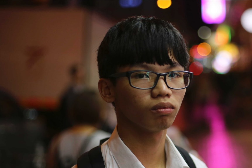 Former Studentlocalism leader Tony Chung wears glasses and looks at the camera as coloured lights shine in the background.