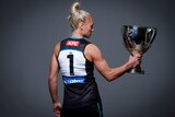 Erin Phillips, with her back to the camera, holds the Premiership Cup to her right and stares into it