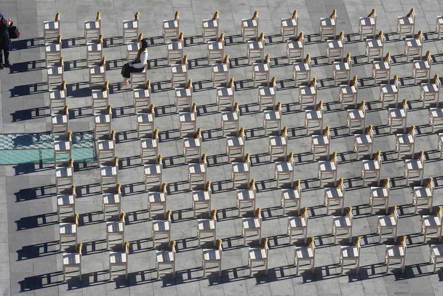 A women takes a photo of a comfort woman statue sitting a chair among rows of empty chairs symbolising victims of comfort women.