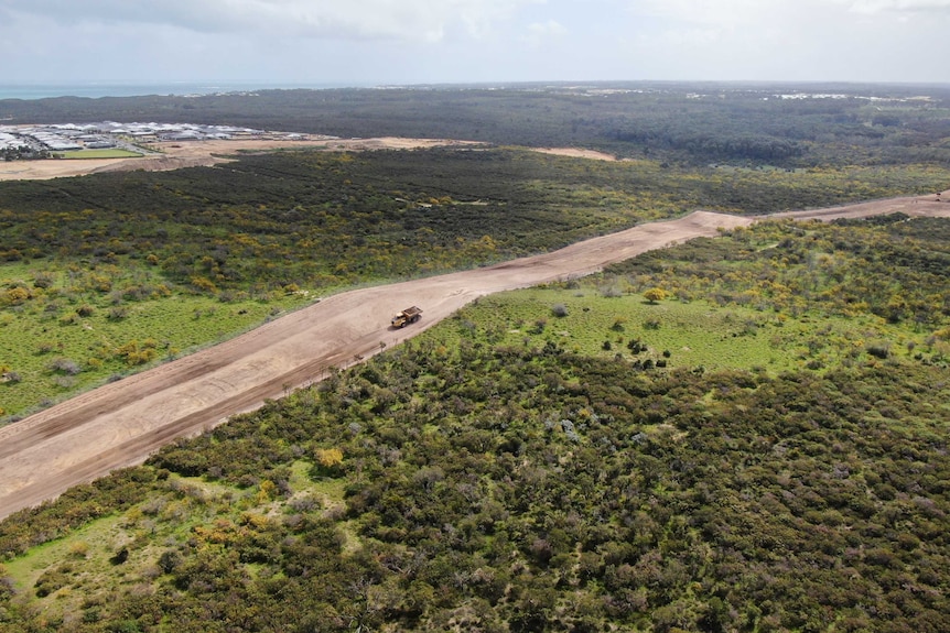 A wide stretch of cleared earth stretches across a green field of scrub land