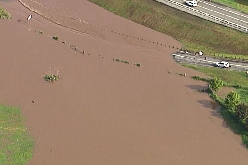 Floodwater flows over a road as cars line up.