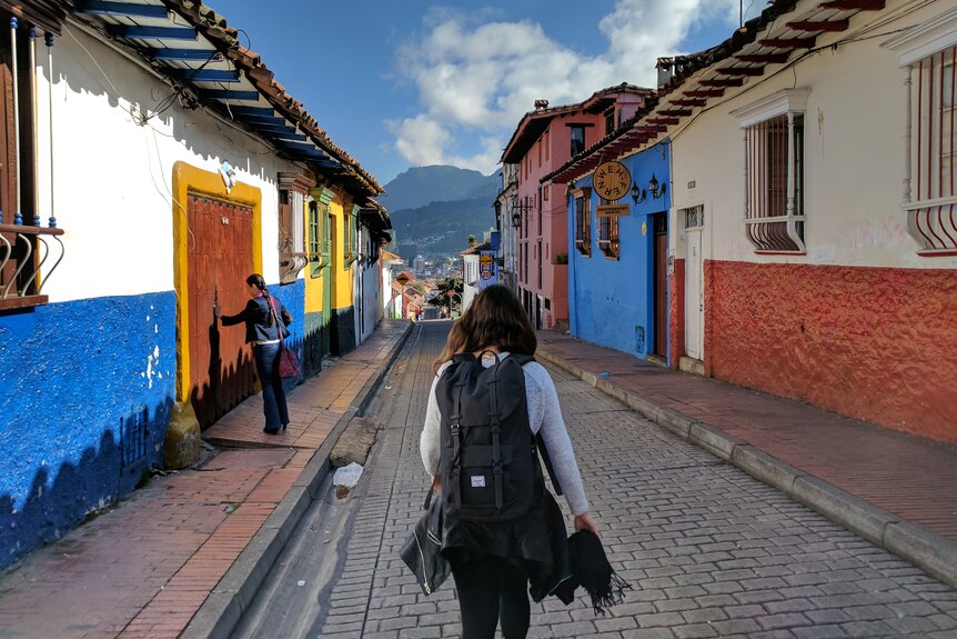 Woman walks down cobbled street with backpack on her back.