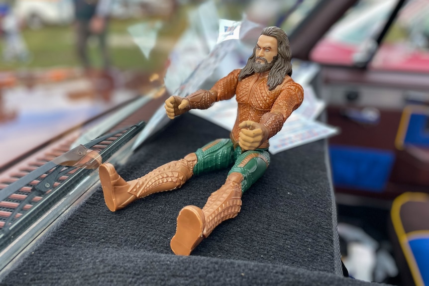 Action figure Aquaman sits on the dash of a car.