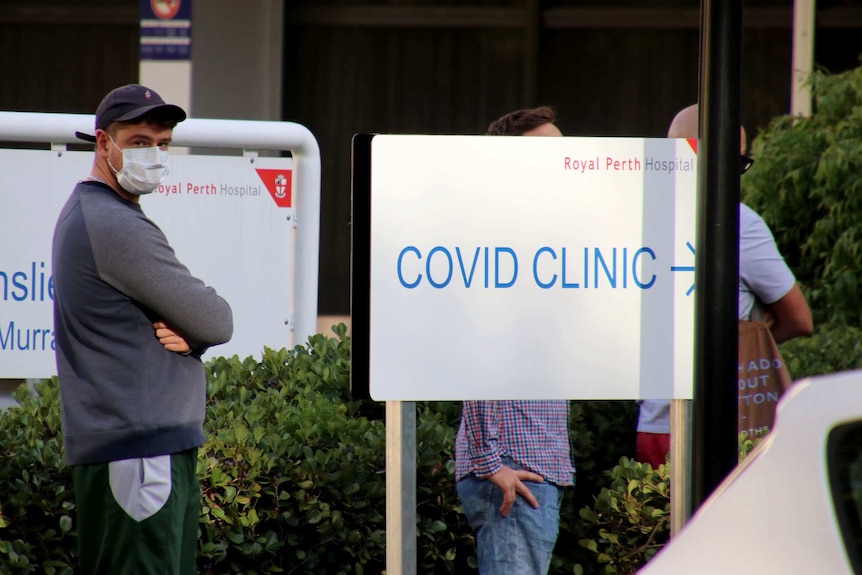A man in a face mask stands next to a sign outside Royal Perth Hospital's COVID-19 fever clinic.