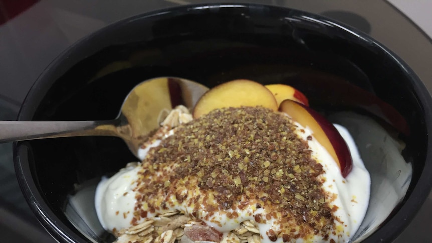 Ground linseed is sprinkled on breakfast muesli with yoghurt in a bowl