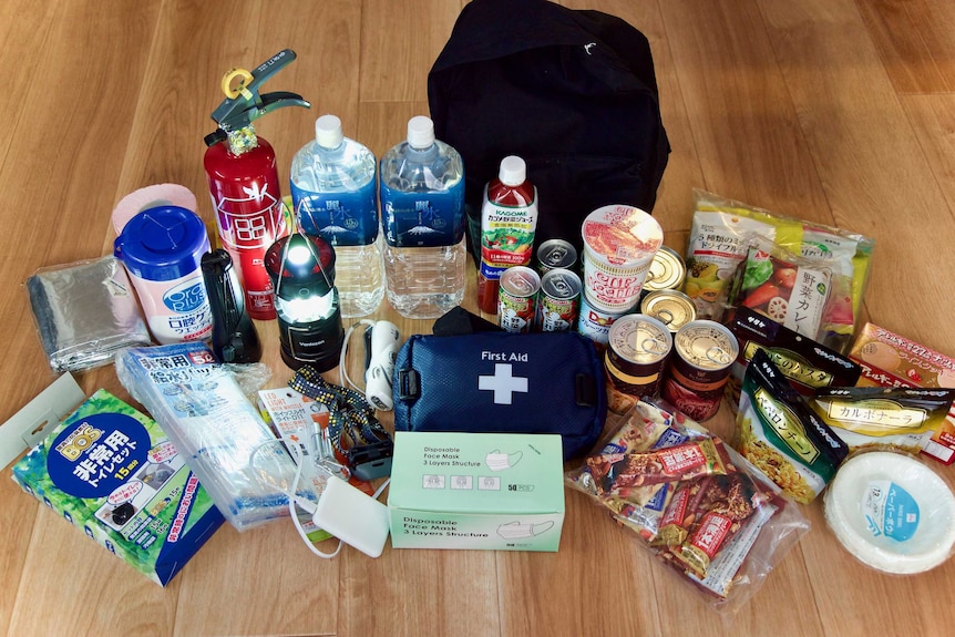 A laid out disaster kit, including first aid supplies, food, face masks, water, a space blanket, a torch and a fire extinguisher