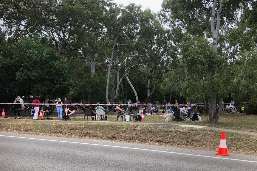 People sit, stand in a park under trees waiting for COVID tests