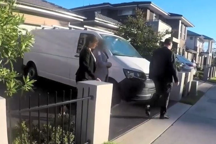 Two plain clothed police officers escorting a woman out of a suburban house.