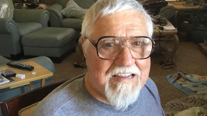 An older man with white hair, a beard and spectacles in his living room.