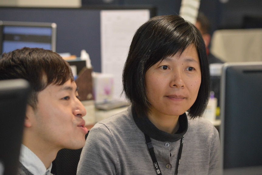 Mo and Xiao faces as they sit next to each other at desk.