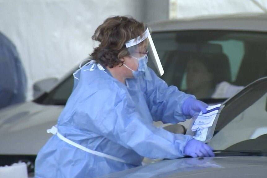 A woman wearing a face mask and visor places a sticker on a car