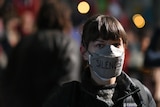 A woman wearing a face mask with the word 'silenced' written on it 