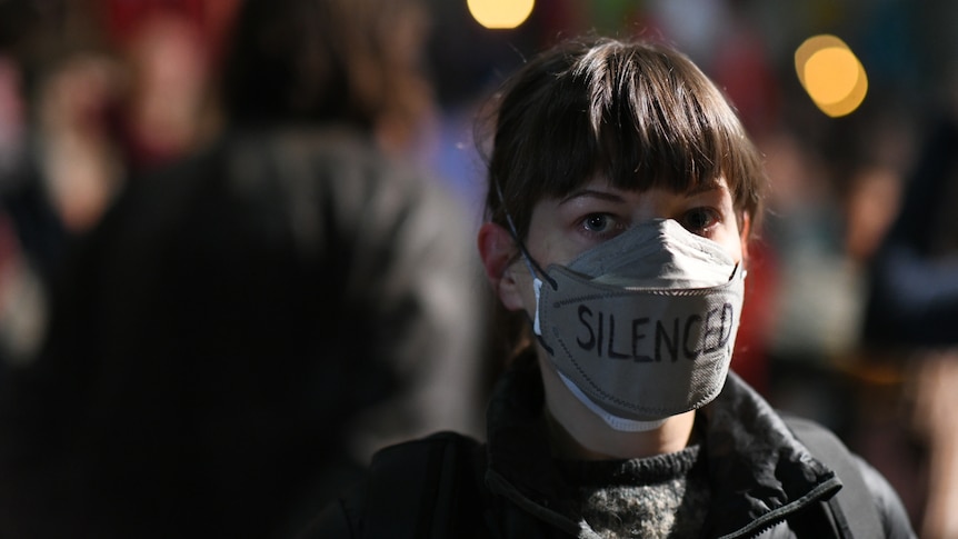 A woman wearing a face mask with the word 'silenced' written on it 