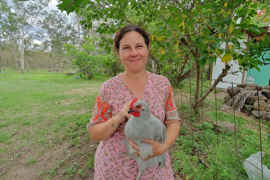 Lady standing in front of a tree holding a chicken