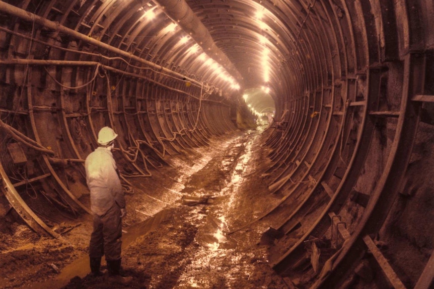 A man stands in mud at the end of a steel tunnel