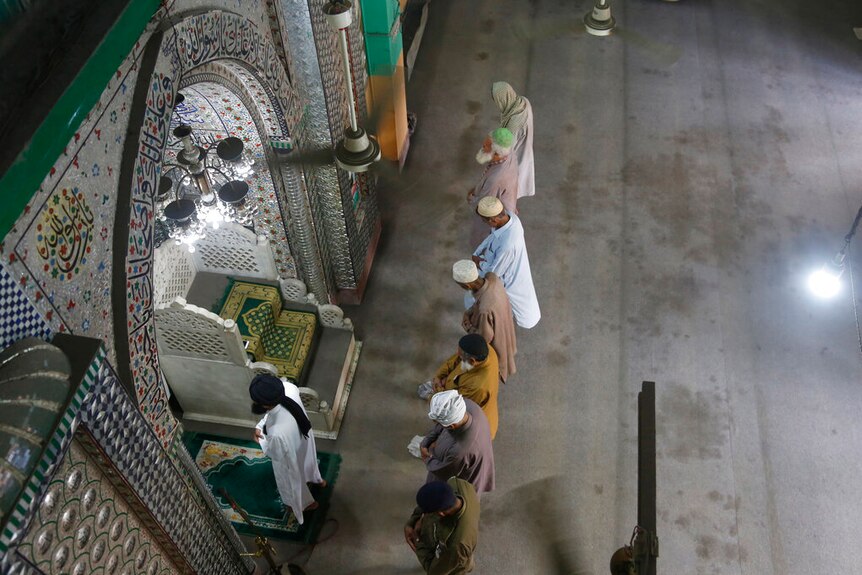 Seven men in robes and caps gather at a mosque to pray. Picture taken from above.