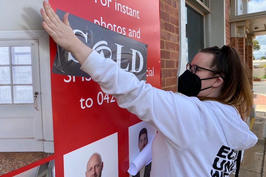 A woman in a white jumper places of a "sold" sticker on a "for sale" sign.