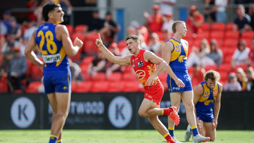 A Gold Coast Suns forward points skywards in celebration after kicking a goal as West Coast defenders look on.