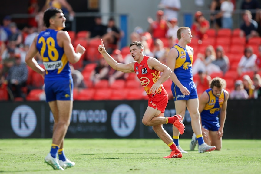 A Gold Coast Suns forward points skywards in celebration after kicking a goal as West Coast defenders look on.