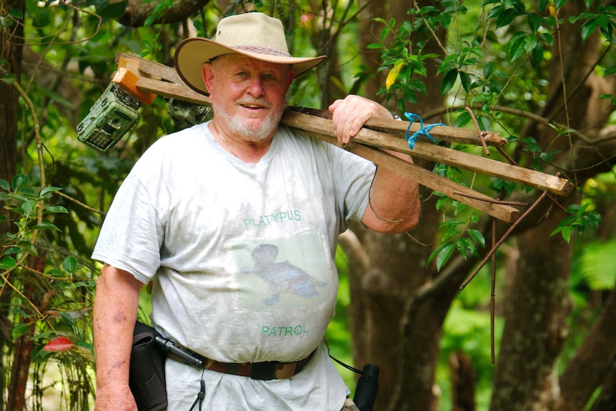 A man in his seventies holds wooden stakes with wildlife camera traps attached to them over his shoulder.
