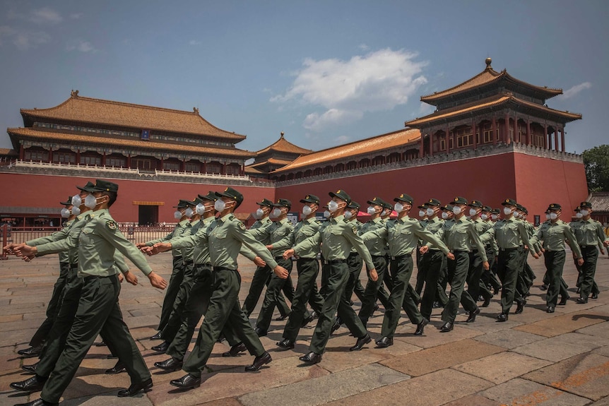 Chinese People's Liberation Army (PLA) soldiers wearing protective face masks march past the entrance to the Forbidden City