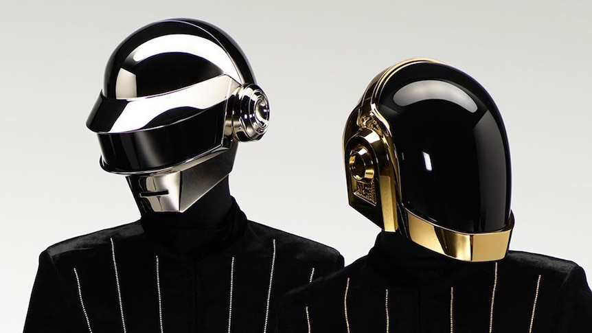 Two members of Daft Punk wearing shiny silver and gold helmets and black suits