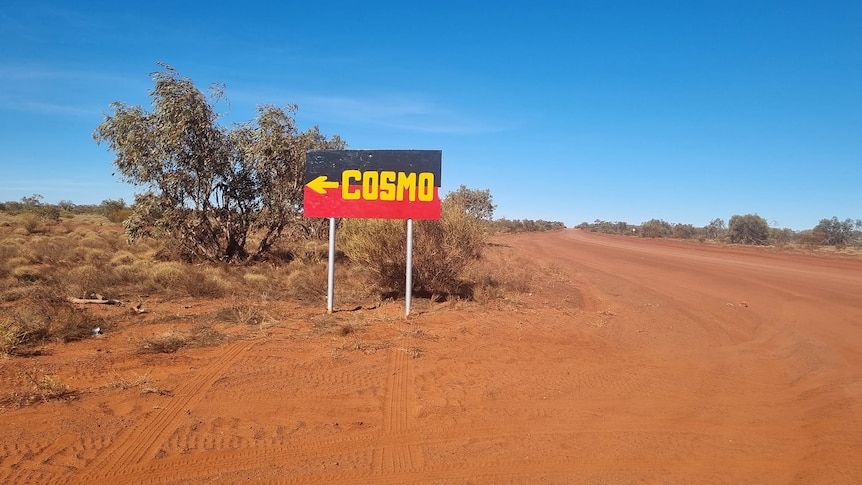 A dirt road with a road sign painted in colours of Aboriginal flag pointing to a remote community.  