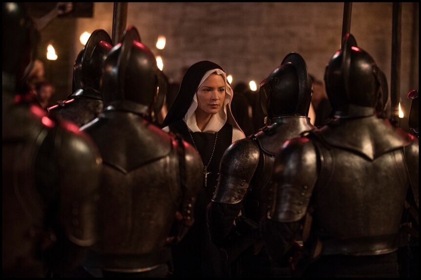 A woman in a nun's habitat is surrounded by soldiers in grey metal body armour.