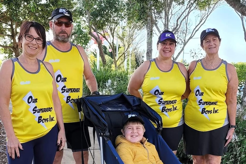 Family wearing matching yellow singles stand around boy in stroller.