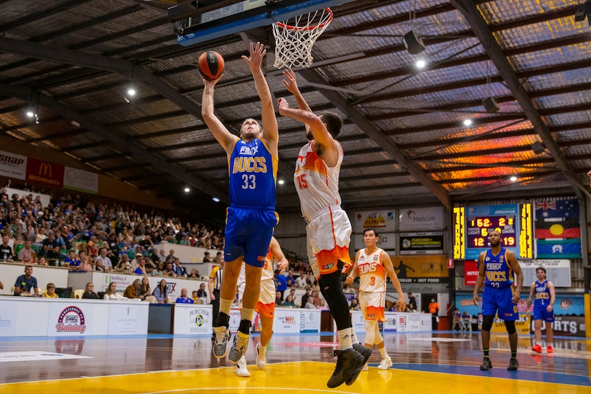 Un homme sautant sous un anneau de basket-ball tire le ballon tandis qu'un autre tend la main pour se défendre