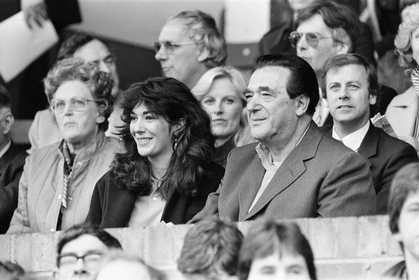Ghislaine Maxwell sits and smiles next to her father, wearing a suit with dark hair,at a football match.