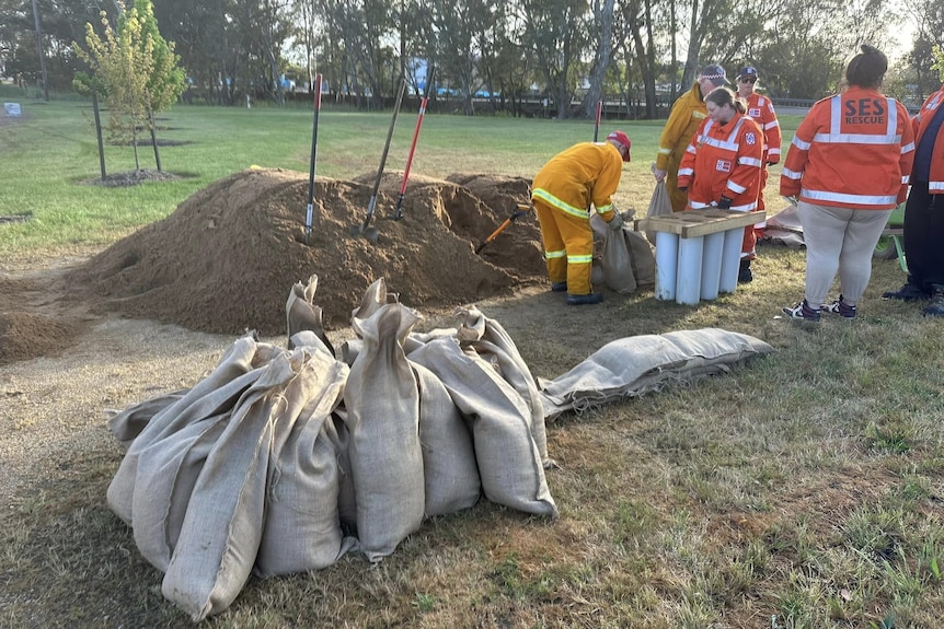 A group of people fill bags with sand. There is a stack of filled bags in the foreground.