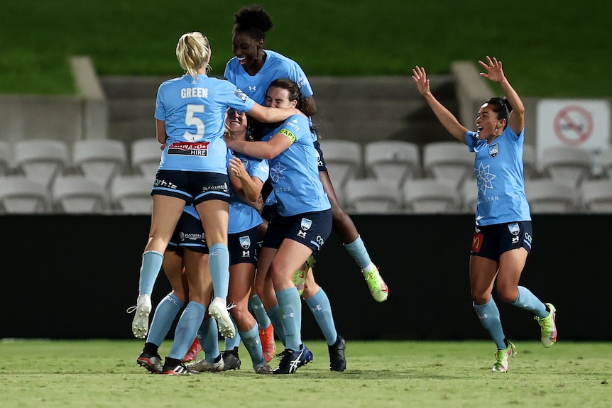 Several Sydney A-League Women players embrace as they celebrate a goal.